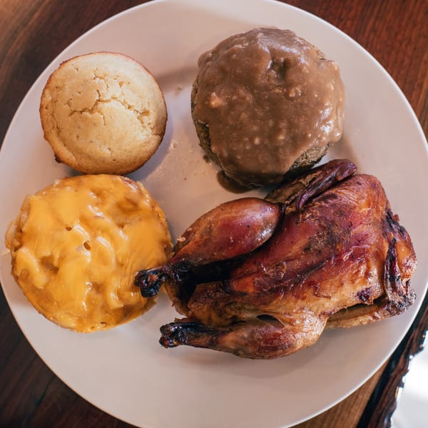 A roasted turkey, mac and cheese, cornbread, and mashed potatoes with gravy on a white plate.