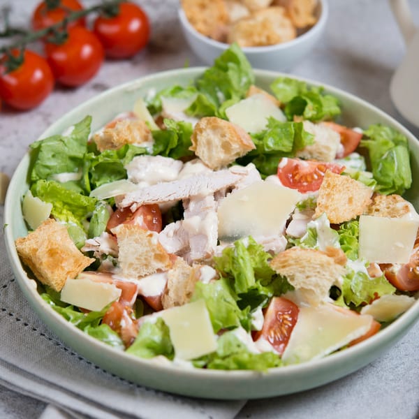 Caesar salad with turkey, croutons, parmesan, and cherry tomatoes in a light green bowl.