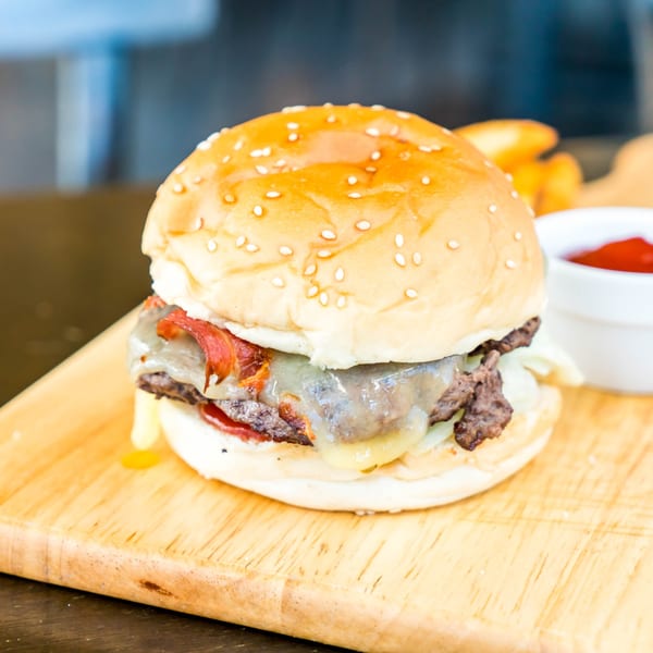 A turkey burger with melted cheese and bacon on a sesame seed bun, served with ketchup.