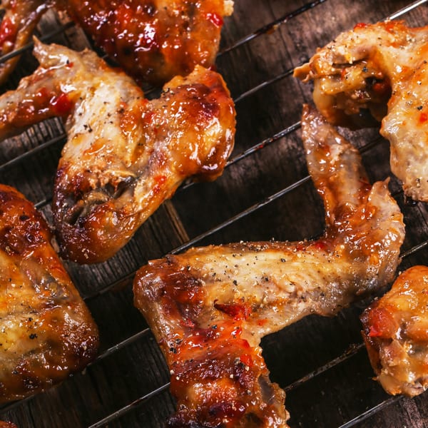 Glazed and seasoned chicken wings cooking on a grill, showcasing The Turkey Grill's soul food.