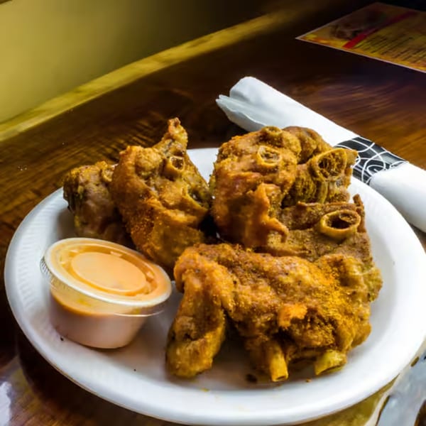 A white plate of golden-brown fried turkey necks with a side of dipping sauce on a wooden table.