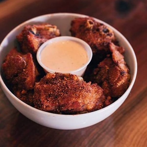 A white bowl filled with crispy, golden-brown fried turkey nuggets and a small cup of dipping sauce.