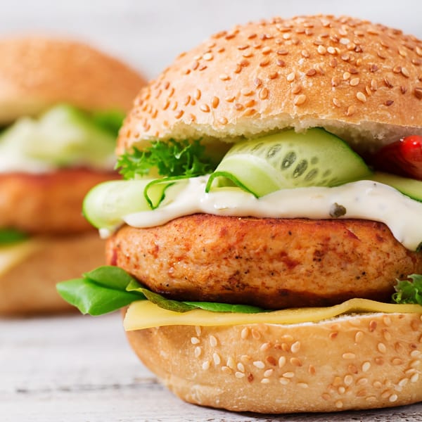 Close-up of a Turkey Grill turkey burger with cheese, lettuce, cucumber, and white sauce.